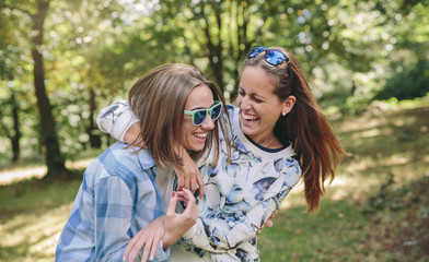 Two happy young women embracing and laughing over a nature background. Friendship and leisure time...