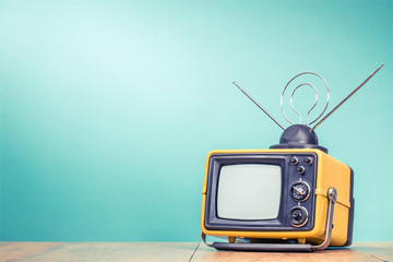 Retro old yellow TV receiver with antenna on wooden table front gradient aquamarine wall background. Vintage instagram style filtered photo