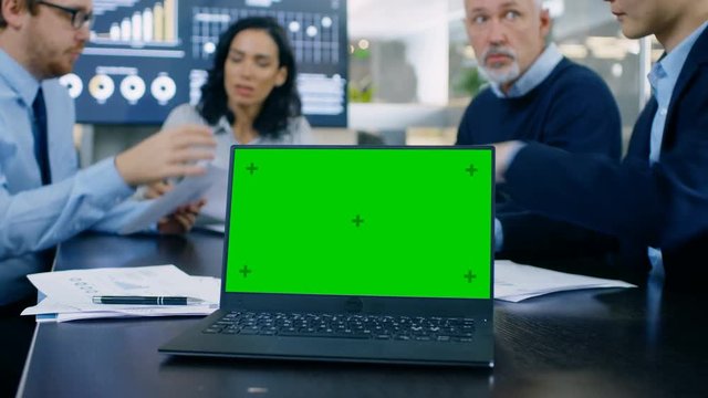 In the Meeting Room Laptop with Green Chroma Key Screen on the Conference Table. In the Background Business People Have Important Discussion. Shot on RED EPIC-W 8K Helium Cinema Camera.