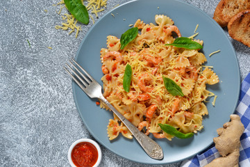 Farfalle with tomato sauce, shrimps and cheese on a concrete background.