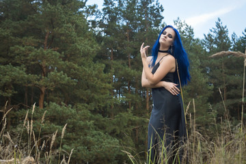 Beautiful woman with dark blue hair dressed in black dress in the magic forest
