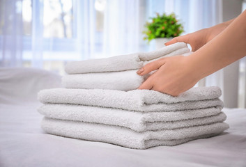 Woman putting white bath towels on bed indoors