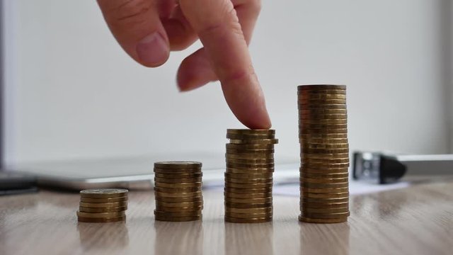 Man hand holding coin dollar on money coin stack arranged as a graph on wooden table. Hand of male or female finger step coins stack growing growth saving money. Business idea.