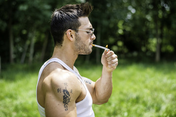 Handsome Muscular Hunk Man Outdoor in City Park or Countryside, Sitting on Grass. Showing Healthy...