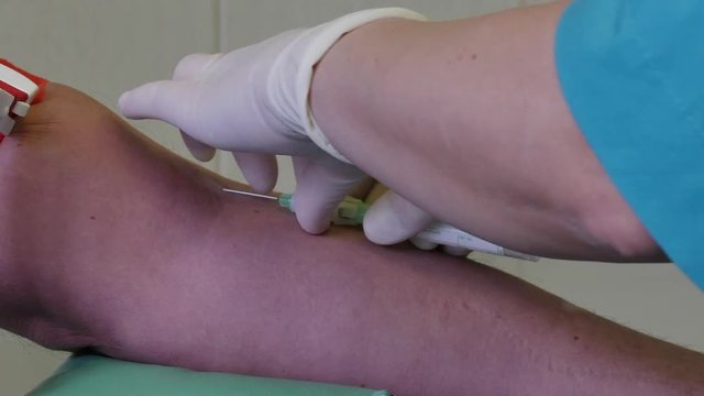 Blood test for analysis and biological research in medical room of clinic. Hands of nurse in sterile gloves stick syringe into vein.
