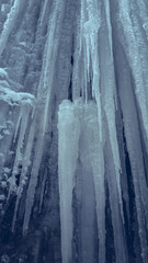 Vertical slippery steep ice wall with long icicles in a cave. Frozen waterfall stream.