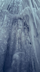 Vertical slippery steep ice wall with long icicles in a cavern. Frozen waterfall stream.