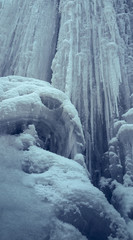 Vertical steep ice wall with long icicles. Frozen waterfall.