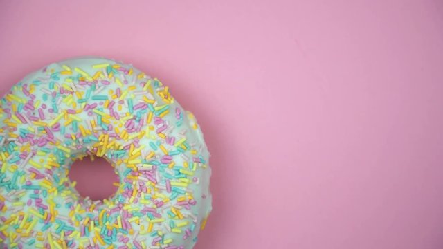 Delicious sweet donut rotating on a plate. Top view. Bright and colorful sprinkled donut close-up macro shot spinning on a pink background.