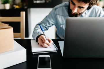 Busy man writing notes in planner at laptop.