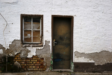 Baufälliges Wohnhaus / Zerbrochene Fensterscheiben und die schiefe Tür eines baufälligen Wohnhauses.