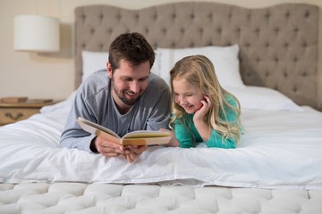 Father and daughter reading a book while lying on bed - Powered by Adobe