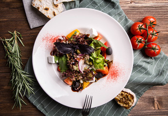 Greek salad with feta on a napkin and dark wooden background