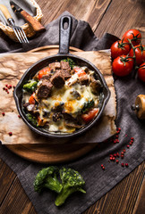 Meat baked with broccoli and vegetables in a black frying pan on a dark wooden background top view