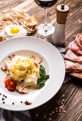 Italian pasta carbonara with bacon and yolk in a white plate on a dark wooden background