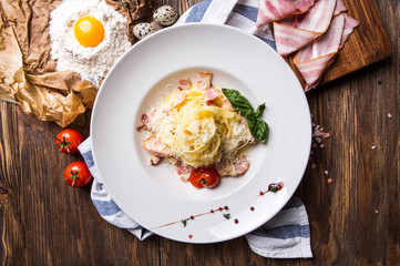 Italian pasta carbonara with bacon and yolk in a white plate on a dark wooden background top view