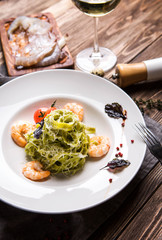 Green pasta with shrimps in a white plate on a dark wooden background top view