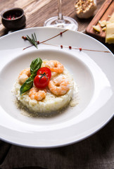 Risotto with shrimps in a white plate on a dark wooden background top view