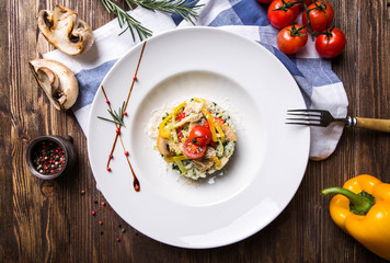 Risotto with vegetables and mushrooms in a white plate on a dark wooden background top view