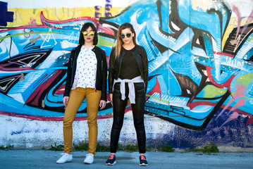 Two pretty girls posing on a spring day in front of graffiti on the wall in background
