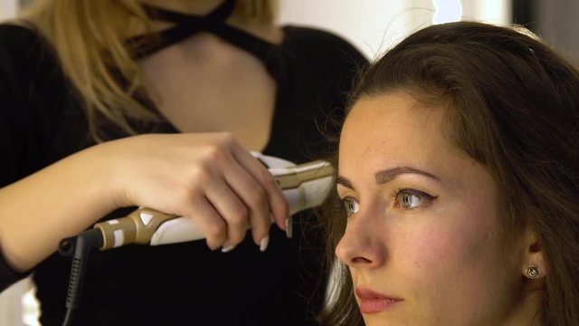 Young beautiful girl in beauty salon. Hairdresser-stylist makes the girl's hair. The hairdresser curls the hair with a styler and stacks them.