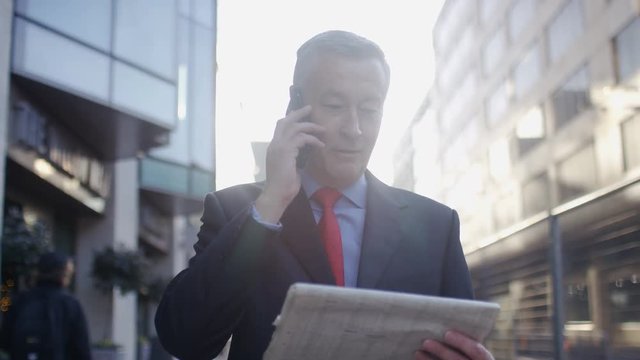 Mature Male Business Man Walking And Talking On His Phone In The City