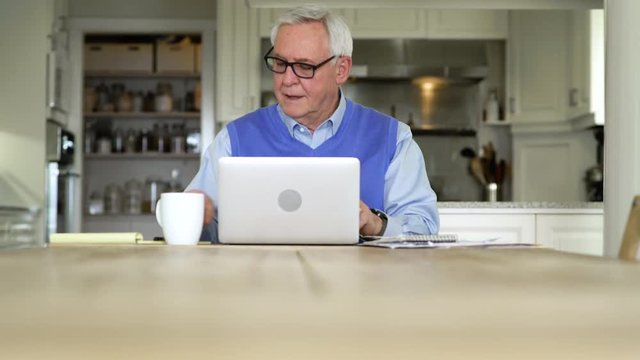 Senior man using a laptop in a dining room