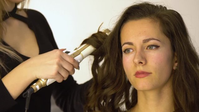 Young beautiful girl in beauty salon. Hairdresser-stylist makes the girl's hair. The hairdresser curls the hair with a styler and stacks them.
