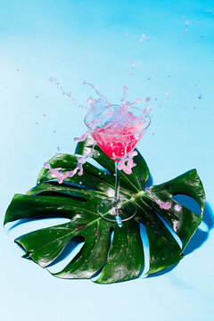 Cocktail spilling from glass on tropical leaf