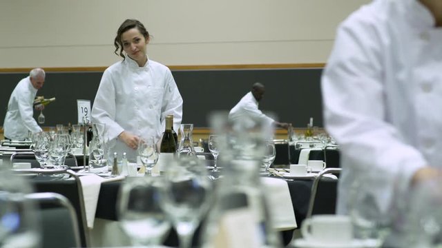 Dolly shot of waiters and waitresses setting tables in a venue