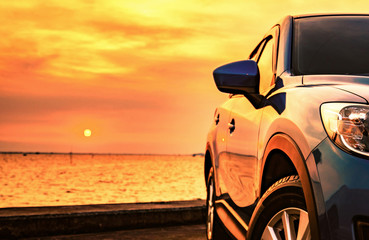 Blue compact SUV car with sport and modern design parked on concrete road by the sea at sunset....
