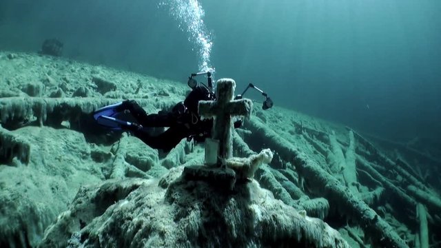 Diver videographer near grave with cross underwaterin Fernsteinsee lake Tyrol. Fernpass in Nassereith Austria.