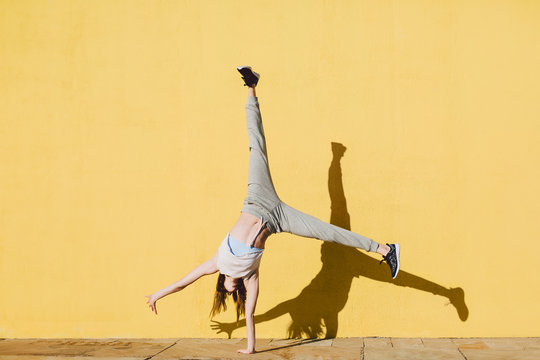 Young woman doing handstand in front of a yellow wall.
