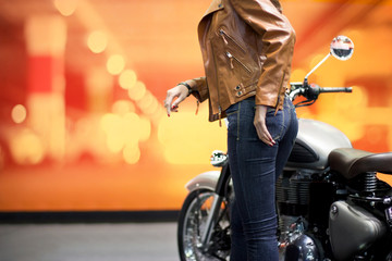 Biker woman in brown leather jacket with a motorcycle on colorful background