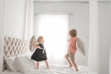 Brother and sister pillow fighting on bed