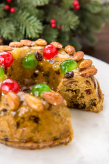 Colorful Christmas fruitcake topped with almonds and glace cherries on white platter