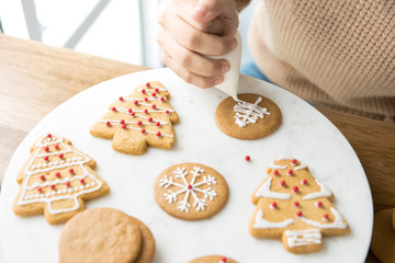 Young woman decorating gingerbread Christmas cookies with royal icing