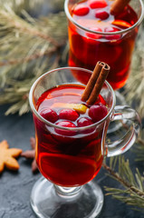 Mulled wine. Christmas hot drink with citrus, apple and spices in a glass cup on a black background.