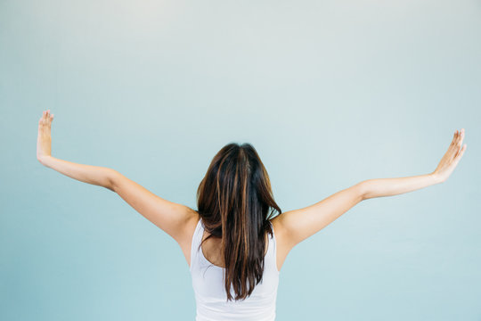 Back Of Beautiful Young Woman With Arms Raised Over Blue Green Background