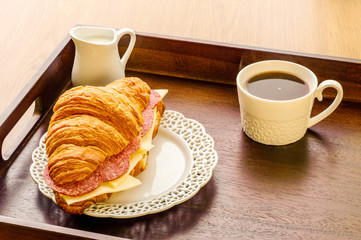 fresh croissant with cheese and sausages cup of black coffee breakfast idea.