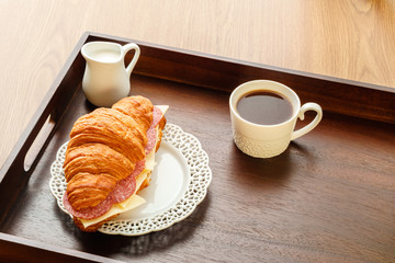 fresh croissant with cheese and sausages cup of black coffee breakfast idea.