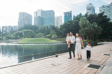 happy stylish parents holding hands with son and daughter walking in sunny street, amazing family moment. father's mother's day