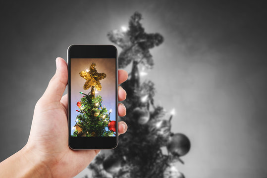 Hands holding mobile smart phone, taking photo of Christmas star on Christmas tree with colorful lights