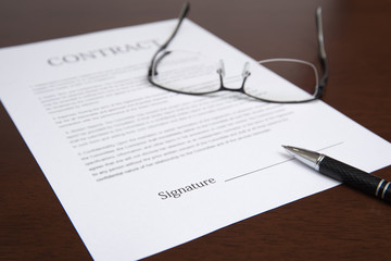 The concept with a contract, glasses, and pen on the desk.  Defocused