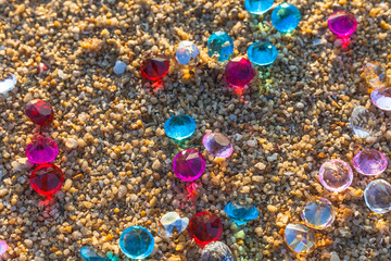 sunshine on the beach in the morning light through gemstones are falling scattered about on the beach.