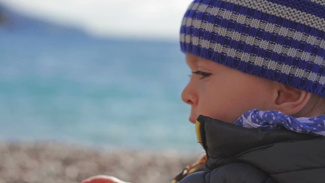 A beautiful little child in a winter hat, playing on the beach with toys.