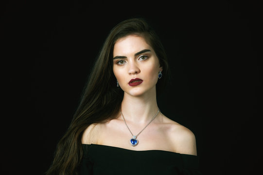 Studio portrait of young beautiful woman with long hair and jewelry on dark background