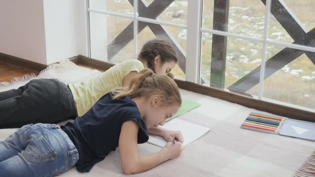 Two cute girls lays on floor and drawing
