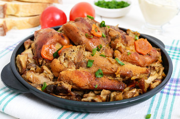 Pieces of fried rabbit with forest mushrooms on a cast-iron frying pan on a white wooden background.