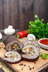 Meatloaf (roll) stuffed with mushrooms, sweet pepper and tomato sauce on a dark wooden background. Festive dish